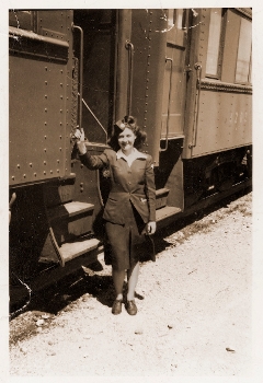 sepia tone photo of woman in 1940s dress standing beside train car